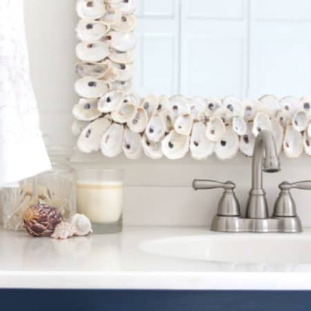 A blue and white color scheme, oyster shell mirror and beach photography give this bathroom a coastal vibe.